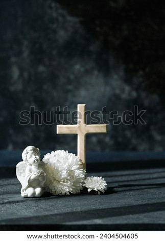 angel baby figurine with white flowers and cross on abstract dark background. concept of faith, Christianity, memory, religion. design template for condolence, mourning card or obituary.