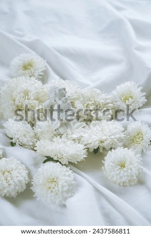 angel figurine and white Chrysanthemum flowers on light fabric abstract background. festive composition with flowers. symbol of faith in God, gentle romantic love