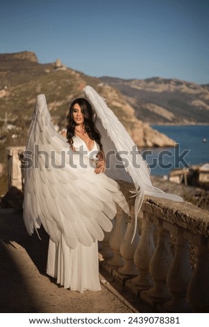 an angel girl with big white wings stands on a mountain at dawn. Early morning, angel on the mountain. The white angel. Sunrise.