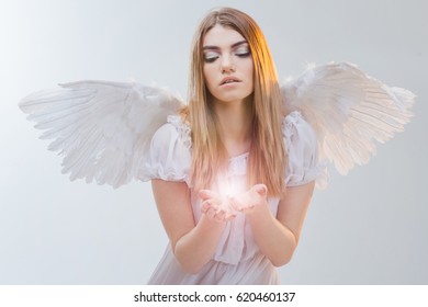 An angel from heaven holding light on the palms. Young, wonderful blonde girl in the image of an angel with white wings.