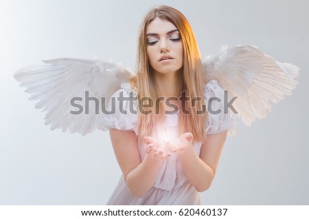 An angel from heaven holding light on the palms. Young, wonderful blonde girl in the image of an angel with white wings.
