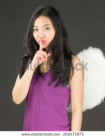 Angel side of a young Asian woman standing with finger on lips asking for silence