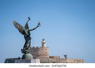 Angel Statue of Victory in Mandraki Harbour in in focus and in the background Saint Nicholas Fortress.