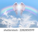 Angel Wings Rainbow Blue Sky Background - pair of angel wings infront of a rainbow arc against a beautiful blue sky with fluffy clouds ideal for a spiritual or religious blessing theme
