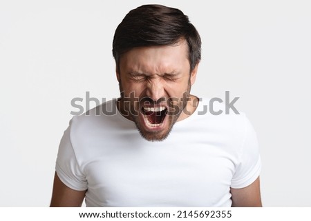 Anger. Mad Male Shouting Loudly In Anger With Eyes Closed Expressing Fury Posing Standing On White Background. Rage, Negative Emotions Concept. Studio Shot