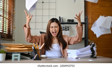 Angered, furious, crazy and mad millennial Asian businesswoman or female office worker screaming, shouting and throwing up papers at her office desk. Depression, overworked, failure. - Shutterstock ID 2204953753