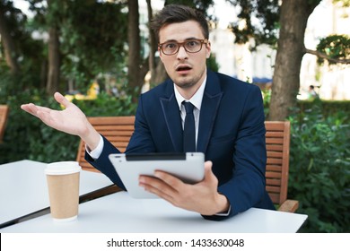 Angered Man In A Suit With An IPad In His Hands Looks Into The Camera And A Cup Of Coffee On The Table