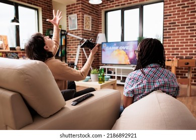 Angered Woman Screaming At Sky Because Of Lost Game Round Of Videogame Played On Gaming Console. Diverse People Sitting On Sofa While Playing Space Simulator Game On Modern Entertainment Device.