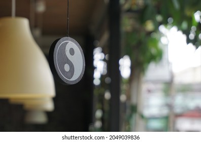 Angle of elevation of a circular wooden plank hang from the ceiling of the eaves. It has a symbol of yin and yang energy of Taoism on its surface. Blurred yellow lanterns and garden in the background. - Powered by Shutterstock