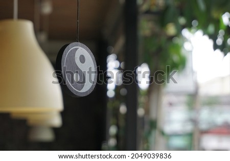 Angle of elevation of a circular wooden plank hang from the ceiling of the eaves. It has a symbol of yin and yang energy of Taoism on its surface. Blurred yellow lanterns and garden in the background.