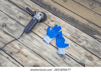 Angle grinder and blue work gloves rest on weathered wooden planks. Tools imply construction, renovation