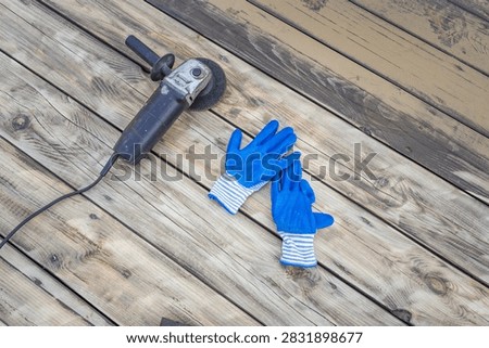 Angle grinder and blue work gloves rest on weathered wooden planks. Tools imply construction, renovation