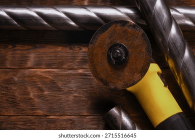 Angle grinder with cutting disc placed among twisted steel pipes on wooden workbench table background.