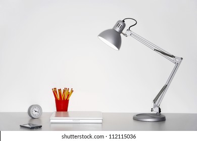 Angle Poise Lamp, Laptop, Clock, Pencil Holder And Cellphone On Desk