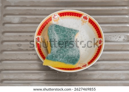 Angle view a dishwashing sponge filled with soap suds, resting in a bowl after cleaning dirty tableware