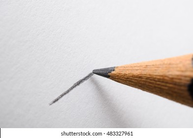 Angled close up (macro) of a graphite pencil drawing a line on textured white paper.