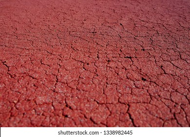 Angled close view of a section of cracked red surface of a playing field.