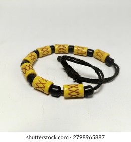 An angled close-up view of a unique handcrafted souvenir bracelet on a bright white background. The design features a continuous strand of yellow resin tube beads with red decorative carvings and small black round beads, emphasizing the braided dark cord loop detail.