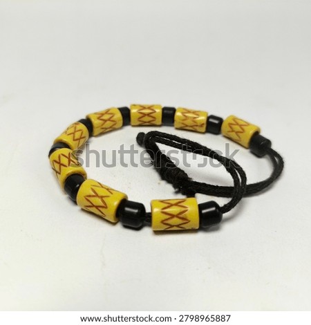 An angled close-up view of a unique handcrafted souvenir bracelet on a bright white background. The design features a continuous strand of yellow resin tube beads with red decorative carvings and small black round beads, emphasizing the braided dark cord loop detail.