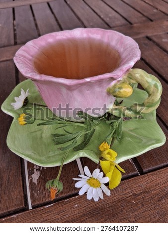 Angled composition of a single decorative tea cup shaped like a flower, with green tea and wildflowers on a wooden table.