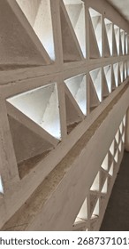 Angled perspective down a concrete breeze block wall with a repeating triangular pattern. Light filters through the openings, creating an abstract architectural background