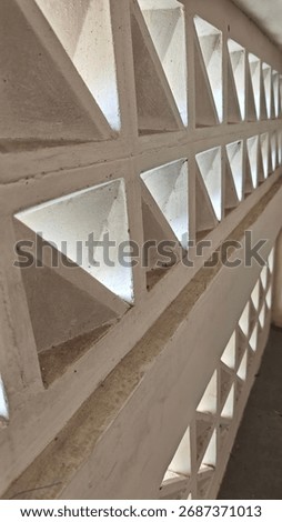 Angled perspective down a concrete breeze block wall with a repeating triangular pattern. Light filters through the openings, creating an abstract architectural background