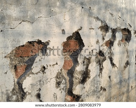 An angled perspective shot of a severely damaged white concrete wall, emphasizing the depth of the cracks, rough texture of peeling plaster, and shadow definition on exposed red bricks