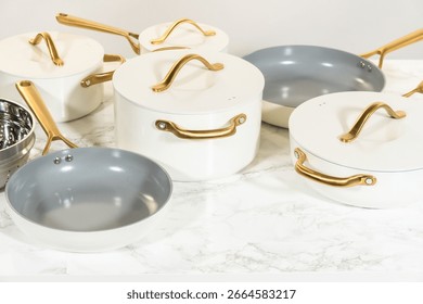 Angled side view of ceramic cookware set with white exteriors and golden handles on a marble countertop. Ideal for cooking blogs, product packaging visuals, or digital marketing use.