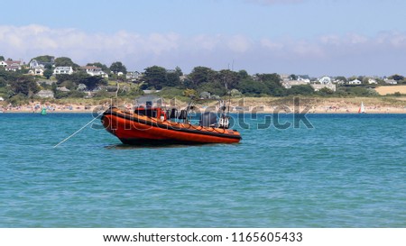 Angled side view of a rigid inflatable boat moored off Cornish coast in the UK on a beautiful hot summers day, clear blue sea water reflecting on the hull and tubes, fishing rods upright in the back. 