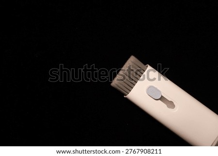 Angled studio capture of a cream cleaning implement, featuring a gray brush head and a side button, against a dark backdrop. Aimed for immaculate spaces.