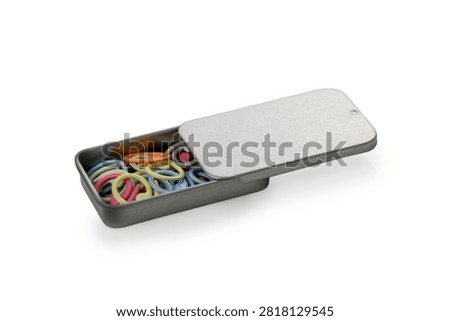 An angled studio product photograph of a rectangular metal tin box with a sliding lid partially closed, filled with an assortment of colorful spiral plastic stitch markers, isolated against a pure white background.