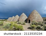 Angled sunny view of the six beehives at Ward Charcoal Ovens State Historic Park, dark cloudy storm skies in background