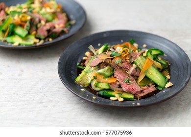 Angled View Of 2 Plates Of Asian Beef Salad. Inspired By Thai And Vietnamese Cuisine, This Salad Is Made With Fresh Healthy Vegetables (carrots, Onions, Cucumber, Etc) And A Nicely Seared Flank Steak