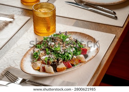 Angled view of beetroot pear and goat cheese walnut salad. High angle close-up of a mixed salad with beetroot, pear slices, cheese, and walnuts in a decorated oval dish.