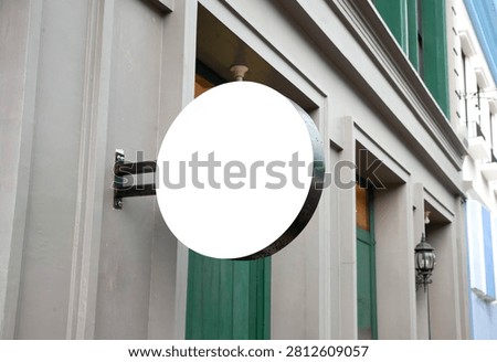 Angled view of a blank white round signboard mockup hanging on a classic style shopfront building wall
