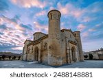 Angled view of the facade of the Romanesque church of San Martín de Tours in Fromista, Palencia, Castilla y Leon, Spain with dawn light and sky of pink clouds