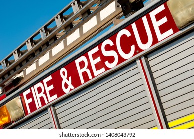 Angled view of FIRE & RESCUE sign on the side of a British ladder and pump fire engine, against a clear blue sky.