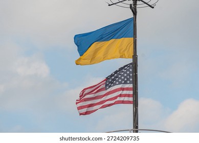 Angled view of a flagpole with two flags blue, yellow and red, white, blue against a cloudy sky Documentary style, no artistic embellishment or distinguishing marks