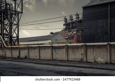 Angled View Of Giant Smoke Stacks Behind A Large Concrete Wall Of An Abandoned Blue Collar Industrial Factory In A Small Rust Belt Town In West Virginia