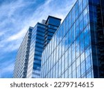Angled view of a large, window covered building corner against a blue, cloud filled sky