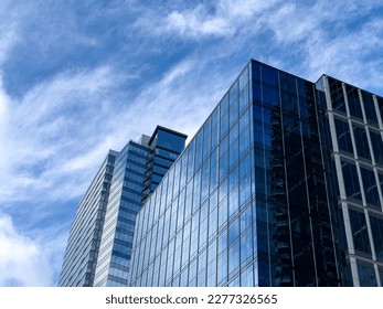 Angled view of a large, window covered building corner against a blue, cloud filled sky - Shutterstock ID 2277326565