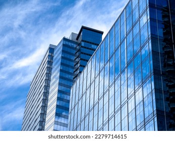 Angled view of a large, window covered building corner against a blue, cloud filled sky