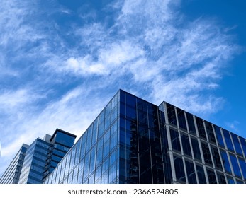 Angled view of a large, window covered building corner against a blue, cloud filled sky