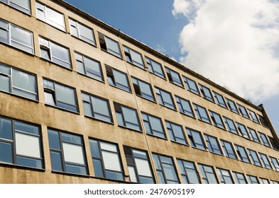 Angled view of a large, window covered building corner against a blue, cloud filled sky.