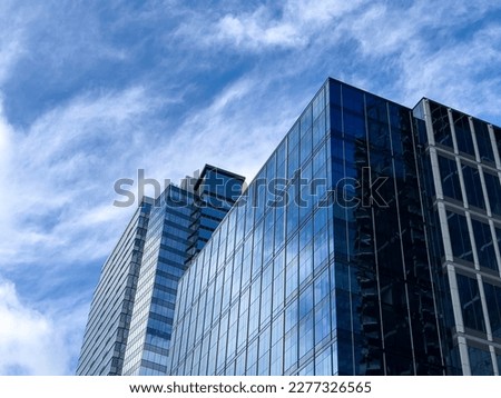 Angled view of a large, window covered building corner against a blue, cloud filled sky