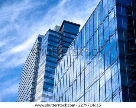 Angled view of a large, window covered building corner against a blue, cloud filled sky