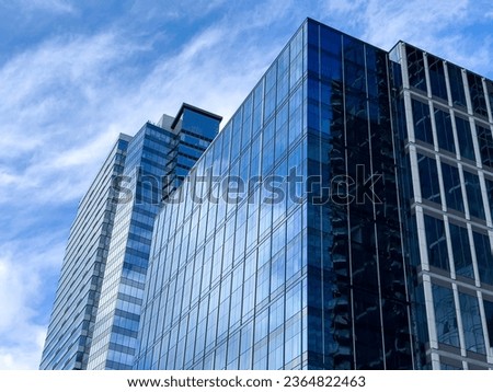 Angled view of a large, window covered building corner against a blue, cloud filled sky