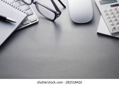 Angled View Of Mac Computer Keyboard And Mouse With Various Office Supplies On Grey Desk With Ample Copy Space