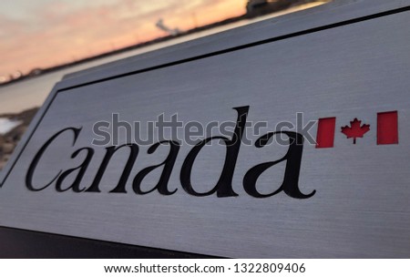 Angled view of the official outdoor Canada sign with Canadian flag. Out of focus blurred sunset sky in the background. Immigration, refugees, asylum seekers, travel, tourism concept.