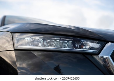 Angled view on headlight of new black car model with basic LED and bulbs version, visible glossy chrome grille frame